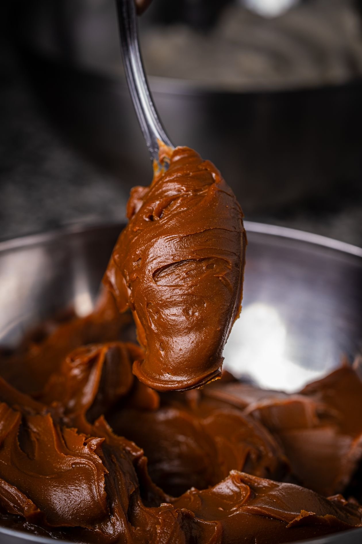 Thick glossy fudge mixture being lifted with a spoon from a mixing bowl