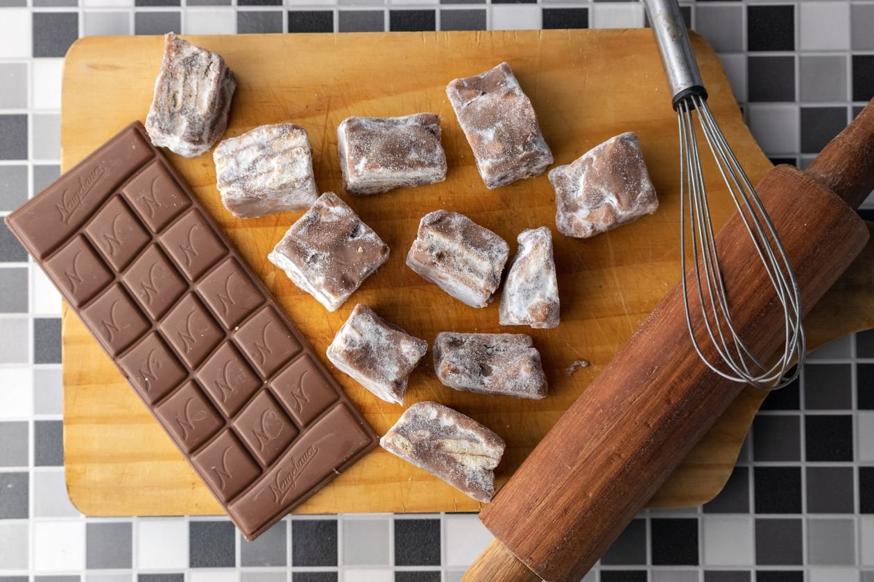 Homemade fudge pieces with a chocolate bar and kitchen tools on a wooden board