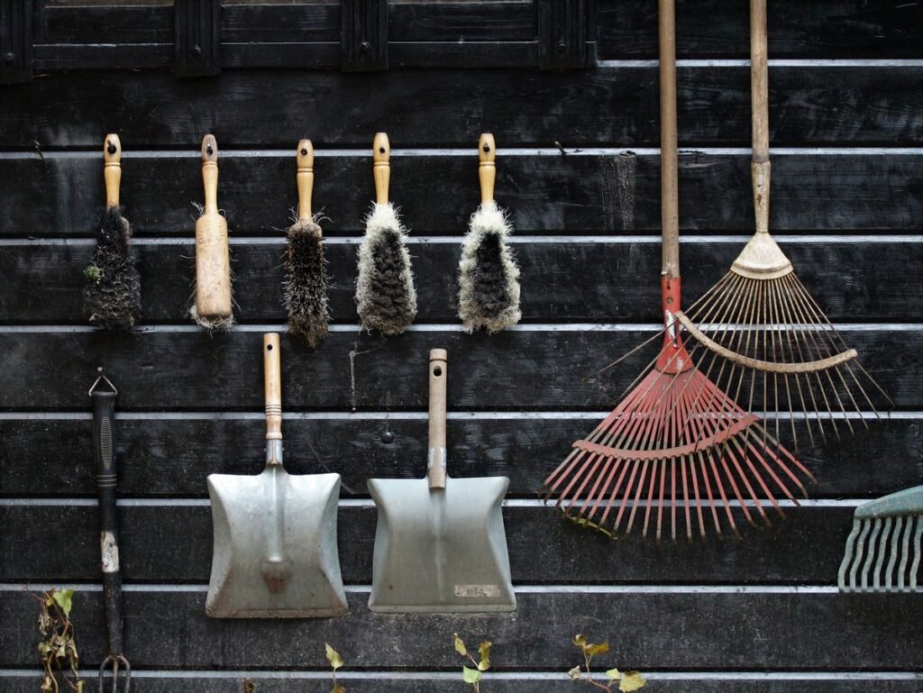 Clean garden tools including rakes brushes and shovels hanging on a shed wall