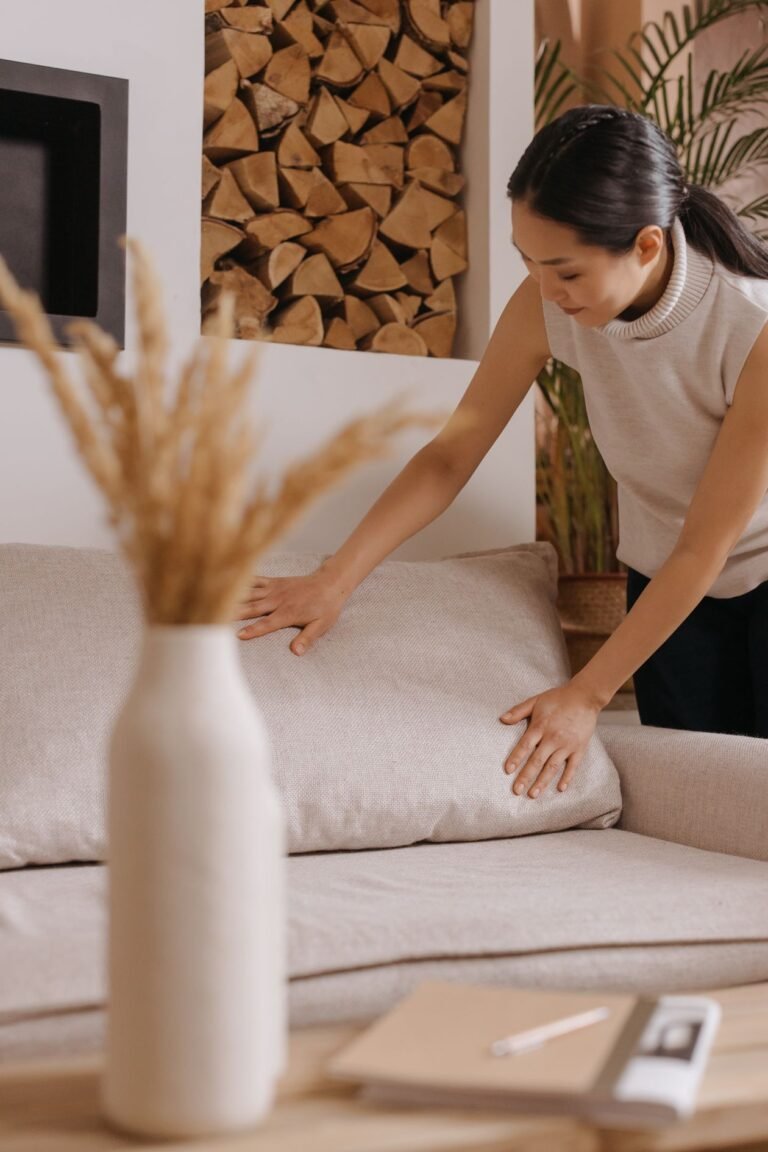 Woman plumping a clean beige fabric sofa cushion in a bright living room