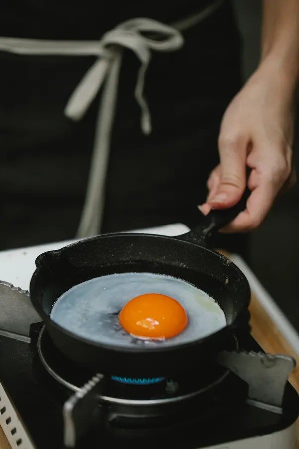 Why Do My Fried Eggs Stick to the Pan and How to Stop It Fried egg cooking in a small frying pan on a gas hob with a hand on the handle
