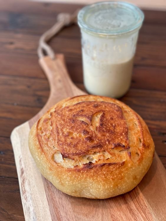 Why Does My Sourdough Starter Smell Like Acetone? 5 Simple Fixes Glass jar of active sourdough starter behind a baked sourdough loaf on a wooden paddle