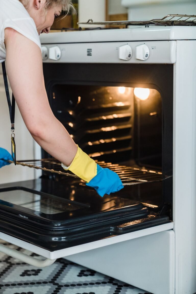 How to Remove Burnt Cheese From Bottom of Oven Woman wearing protective rubber gloves removing an oven rack while cleaning the oven