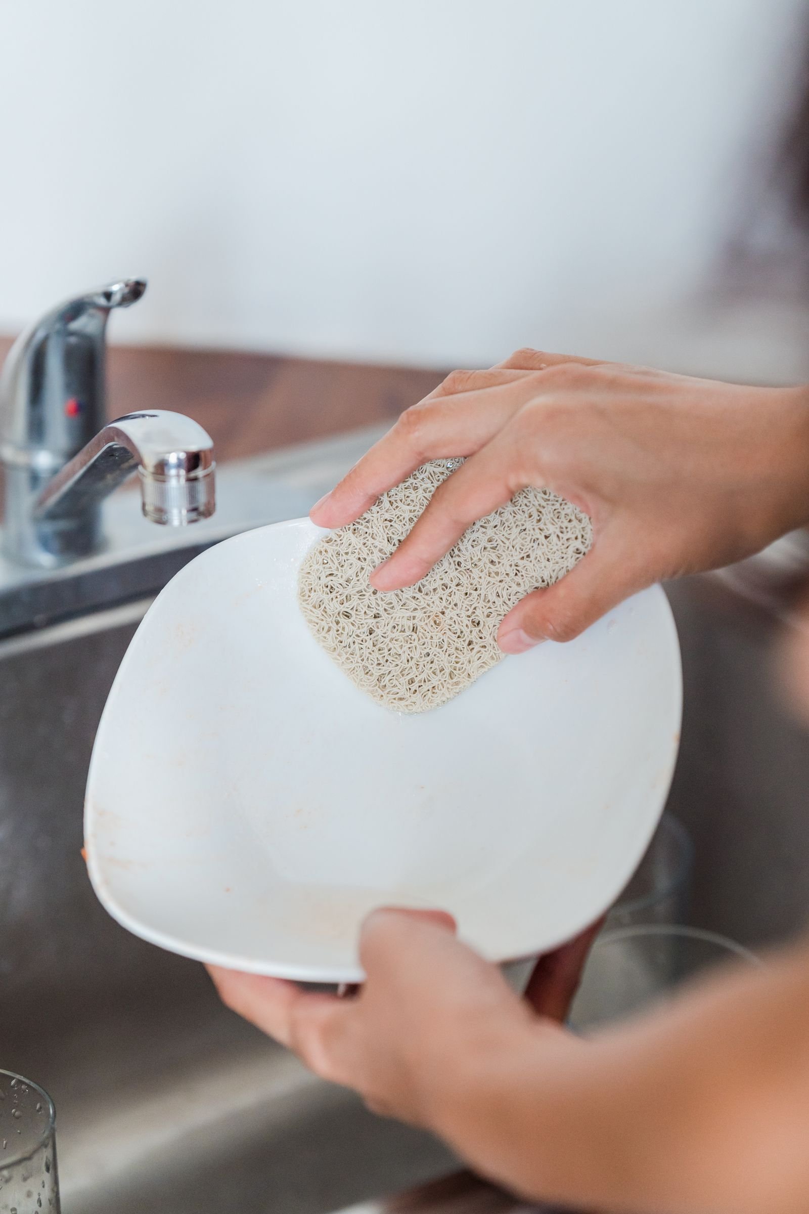 Hand scrubbing a white plate with a sponge at the kitchen sink