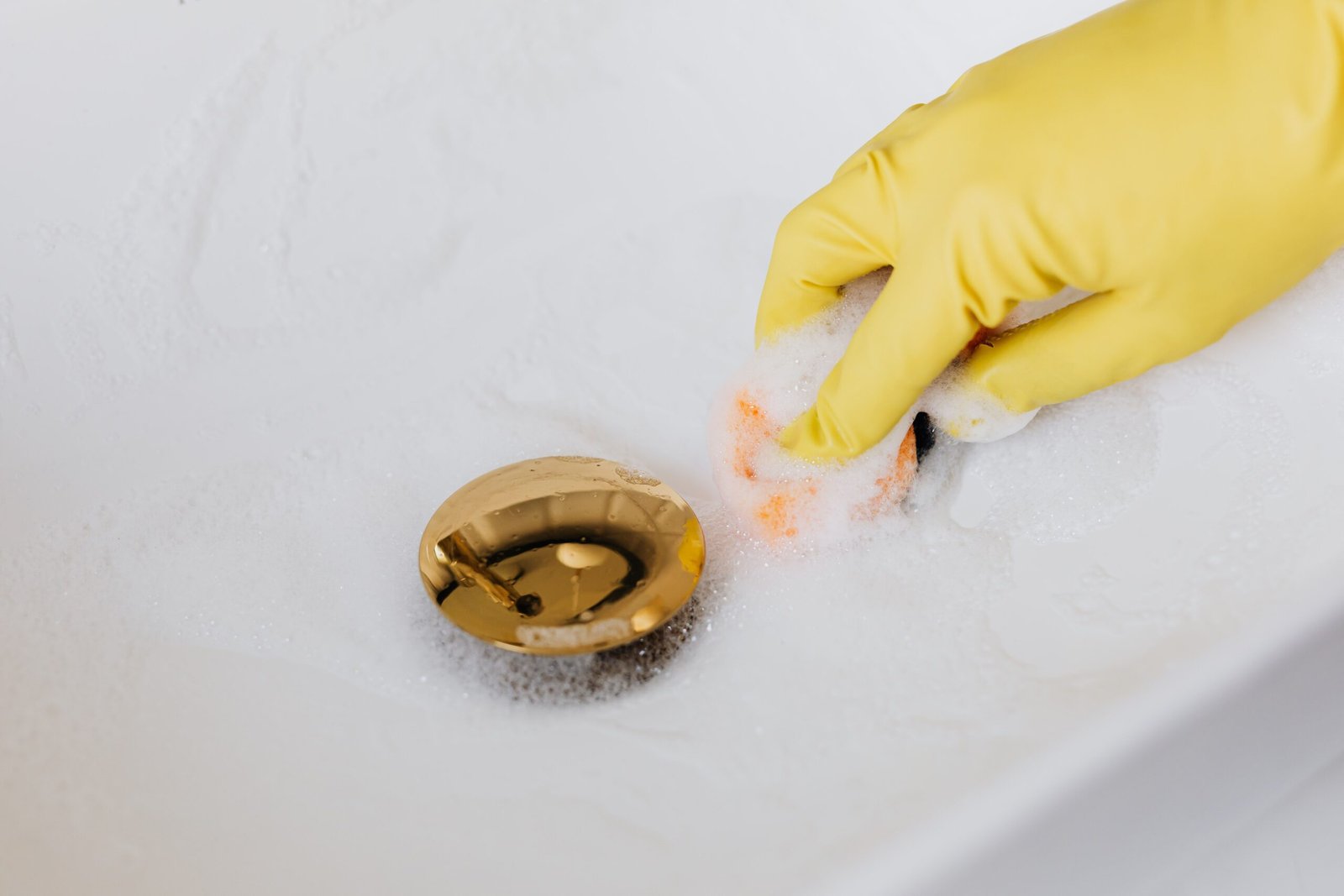 Person in yellow gloves scrubbing a white bathroom sink with a sponge