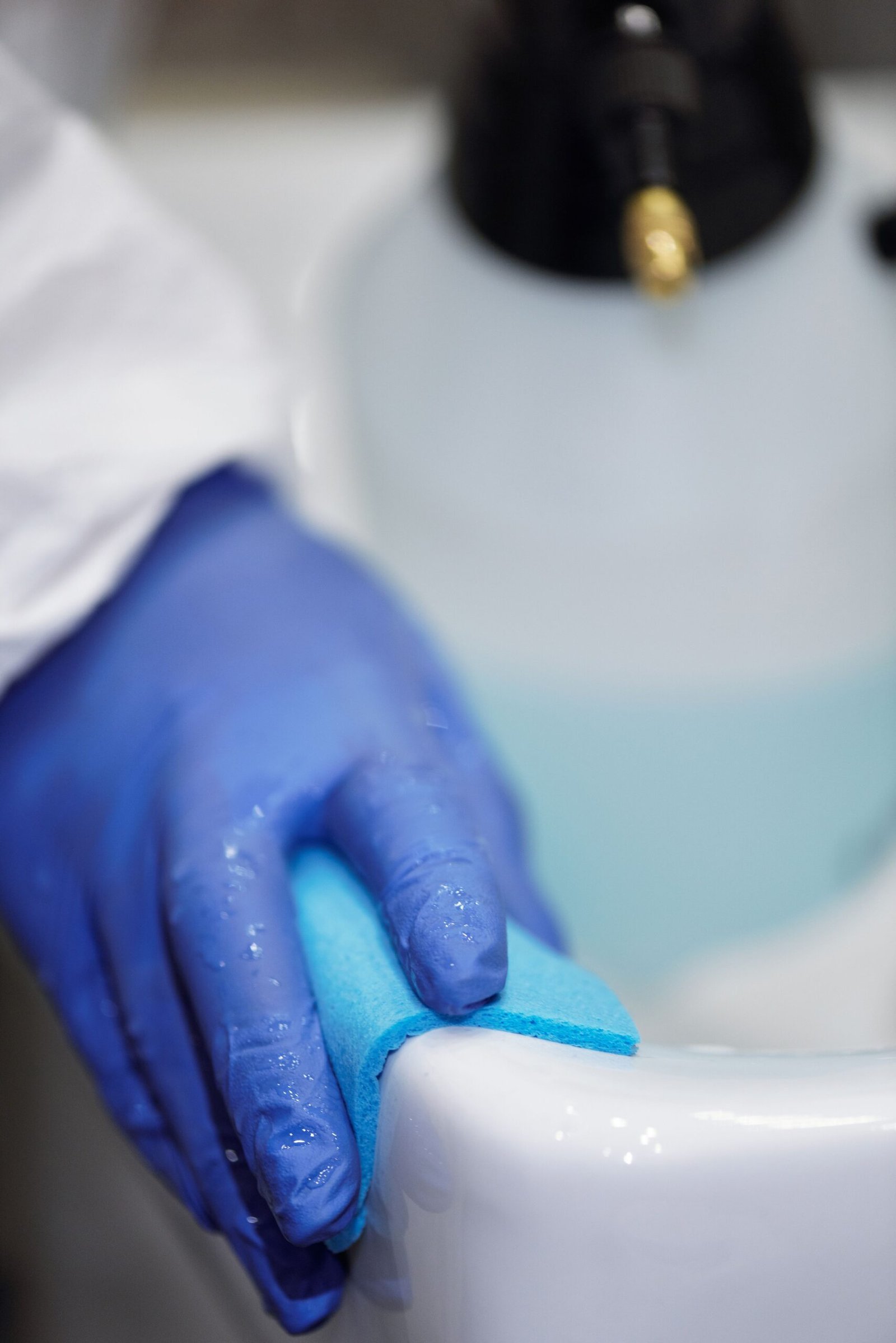 Person in blue gloves cleaning around a bathroom sink drain