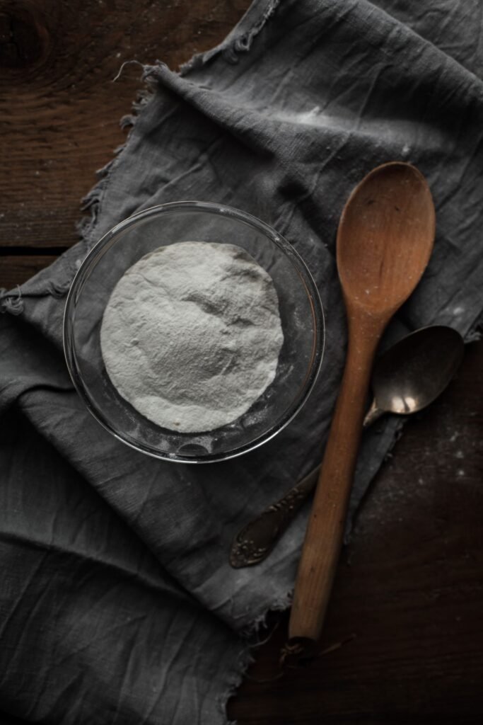 Glass bowl of white bicarbonate of soda powder with wooden spoons on a dark cloth