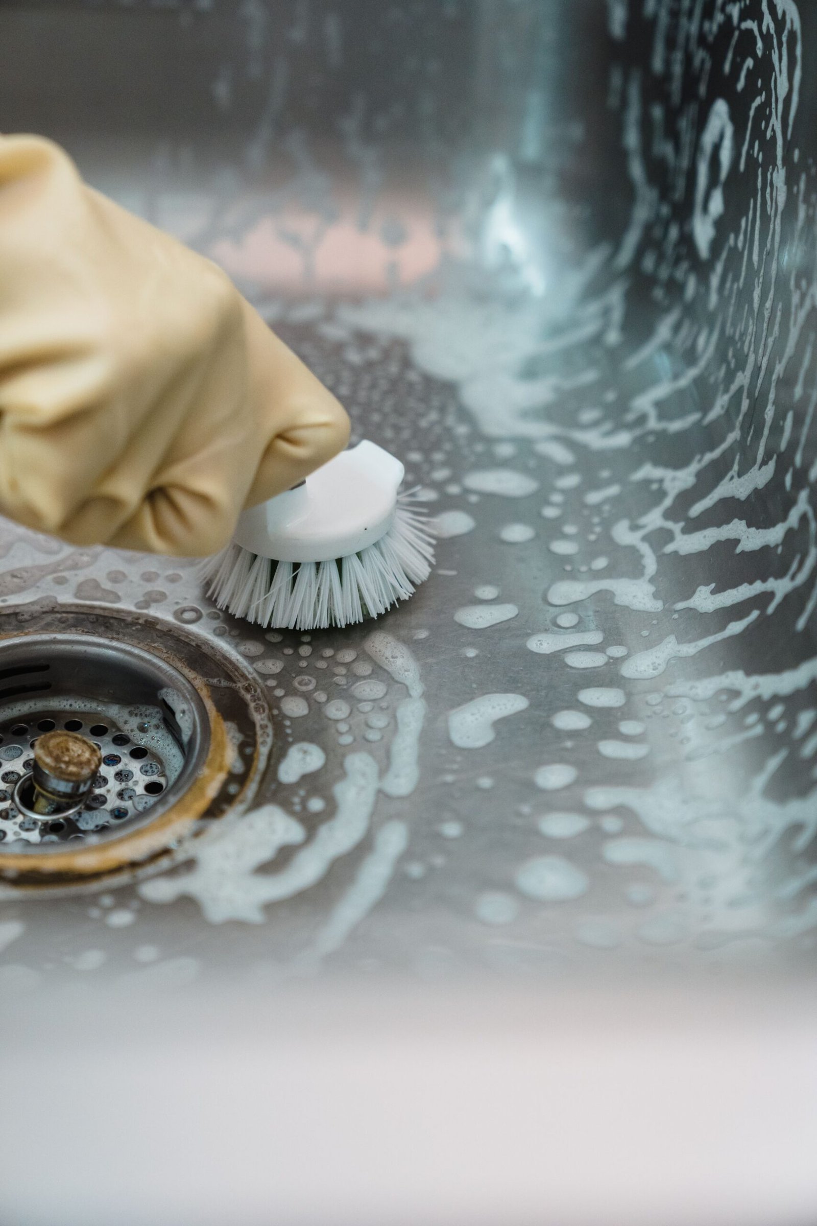 Hands in yellow rubber gloves wiping down a sink basin