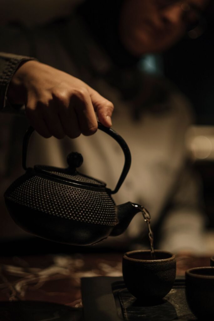 Person pouring fresh tea from a black teapot into small cups after descaling the kettle