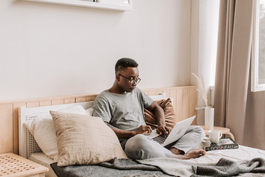 Man using a laptop while sitting on a bed with soft bedding