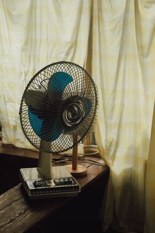Small desk fan on a wooden table beside a window curtain