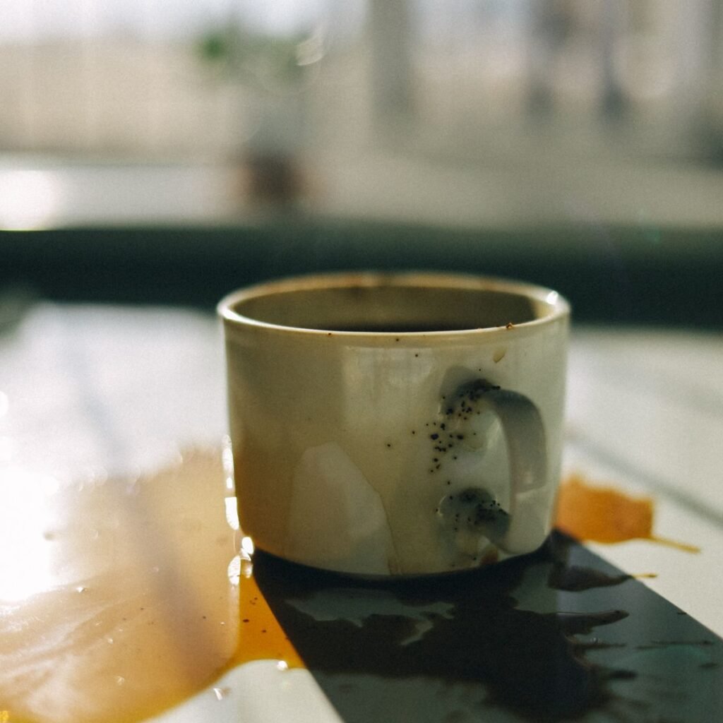 Spilled coffee spreading across a white tabletop next to a cup