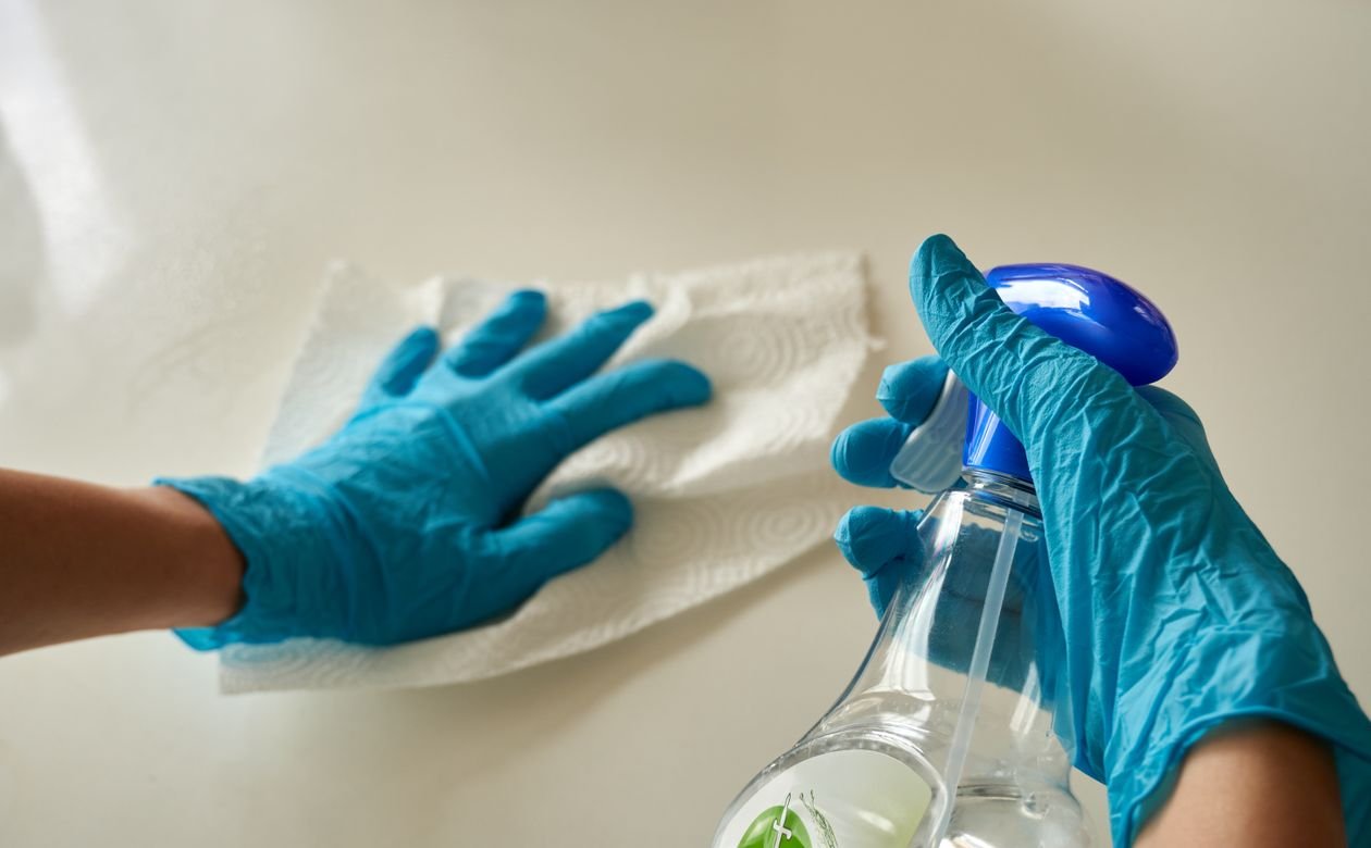 Person wearing blue gloves cleaning with a spray bottle and paper towel