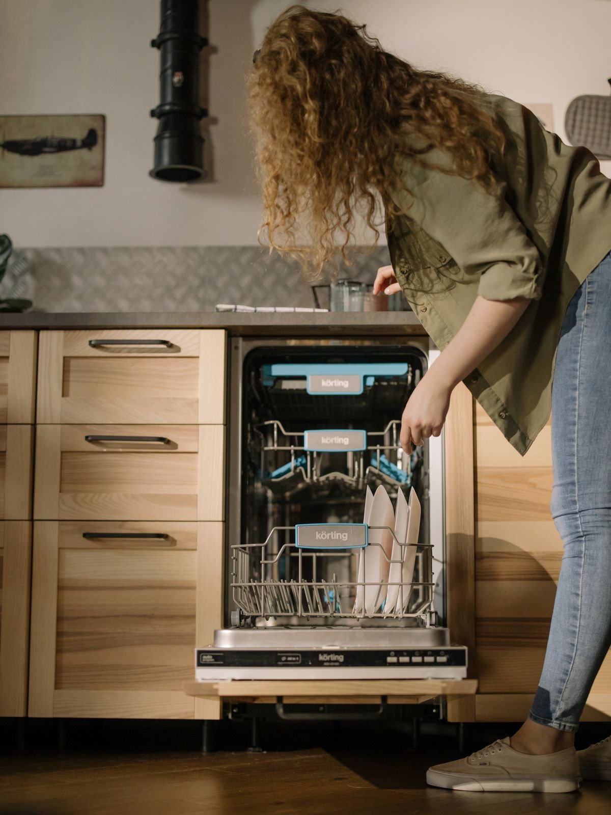 Woman loading clean plates into an open dishwasher