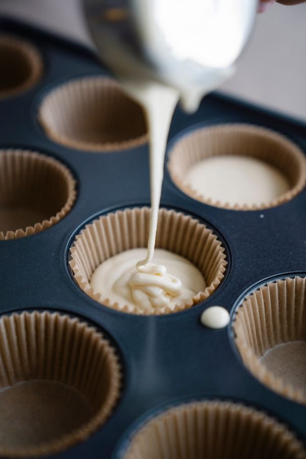 Pouring muffin batter into paper liners in a muffin tin