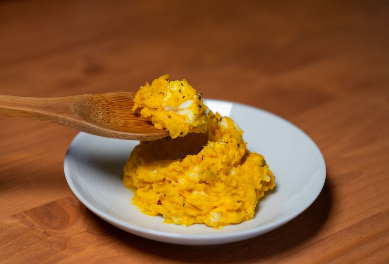 Creamy mashed pumpkin served on a white plate with a wooden spoon
