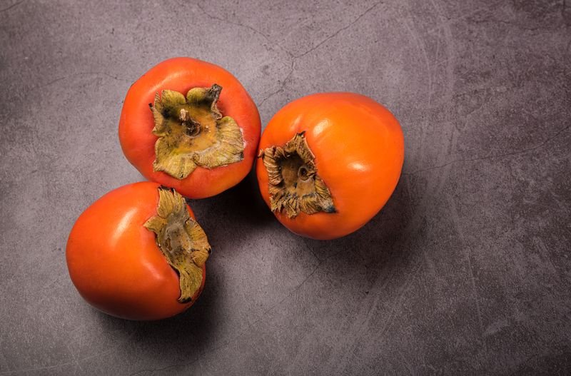 Three whole persimmons viewed from above on a gray stone surface