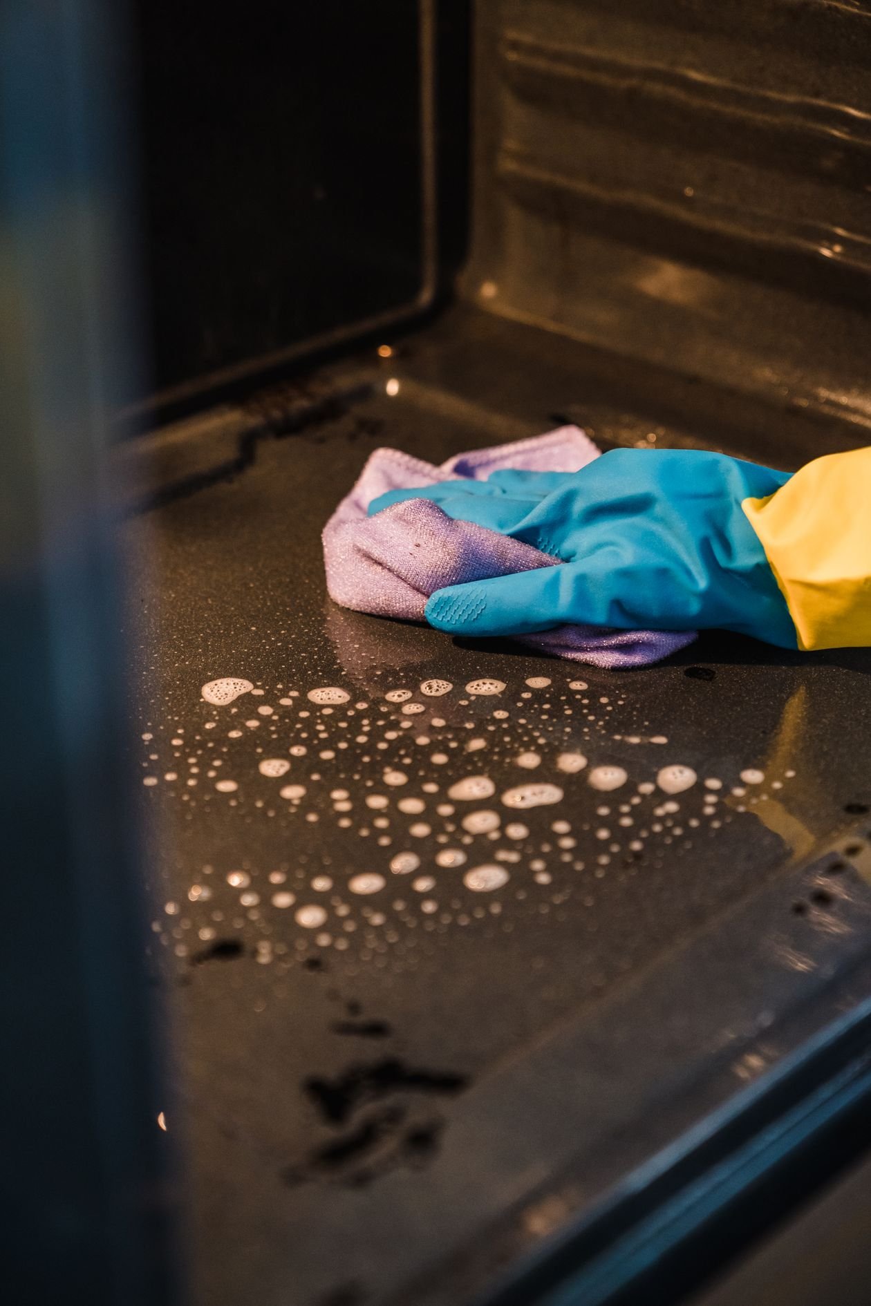 Gloved hand wiping the oven floor with a soapy cloth