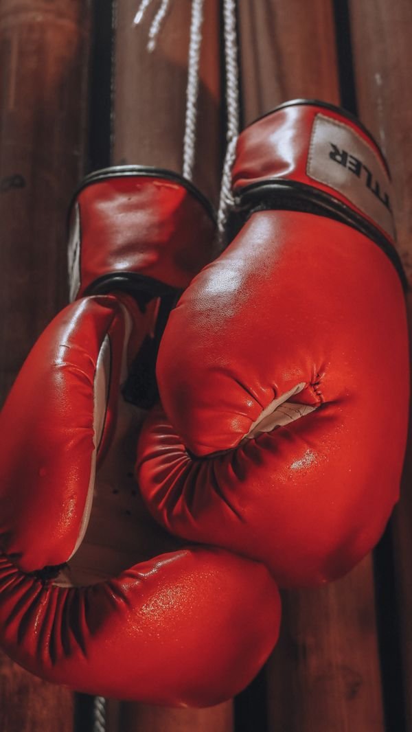 Pair of red boxing gloves hanging from a rope in a gym