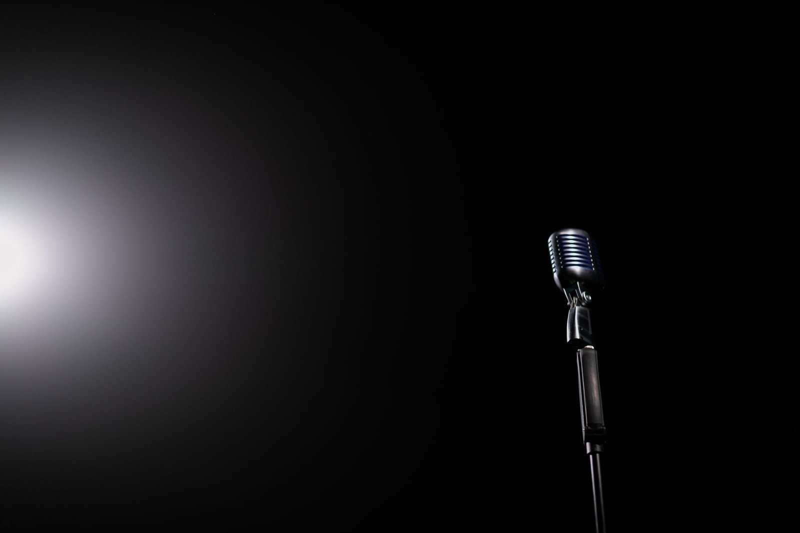 A vintage style microphone lit by a single spotlight on a dark stage, a nod to Miranda Hart stand up comedy roots