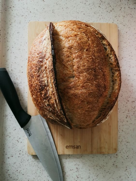 Freshly baked sourdough loaf on a wooden cutting board with a bread knife