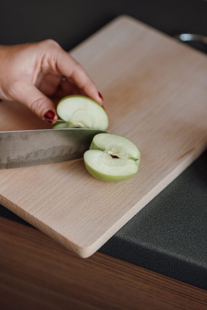 Hand cutting a green apple into slices on a wooden chopping board