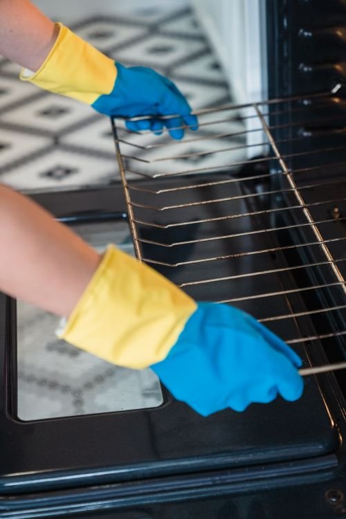 Person removing an oven rack from an open oven before cleaning
