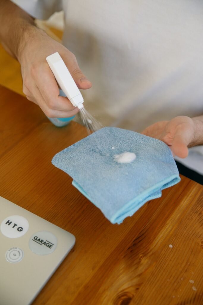 Hands spraying cleaning solution onto a blue microfiber cloth over a table