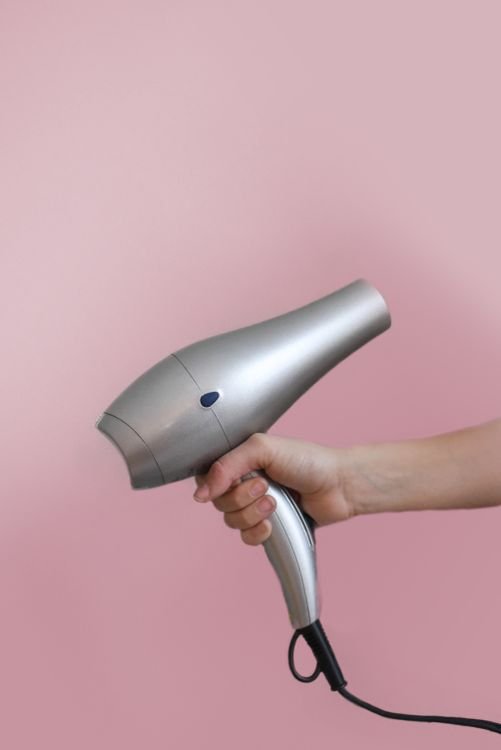 Hand holding a silver hair dryer for melting wax residue