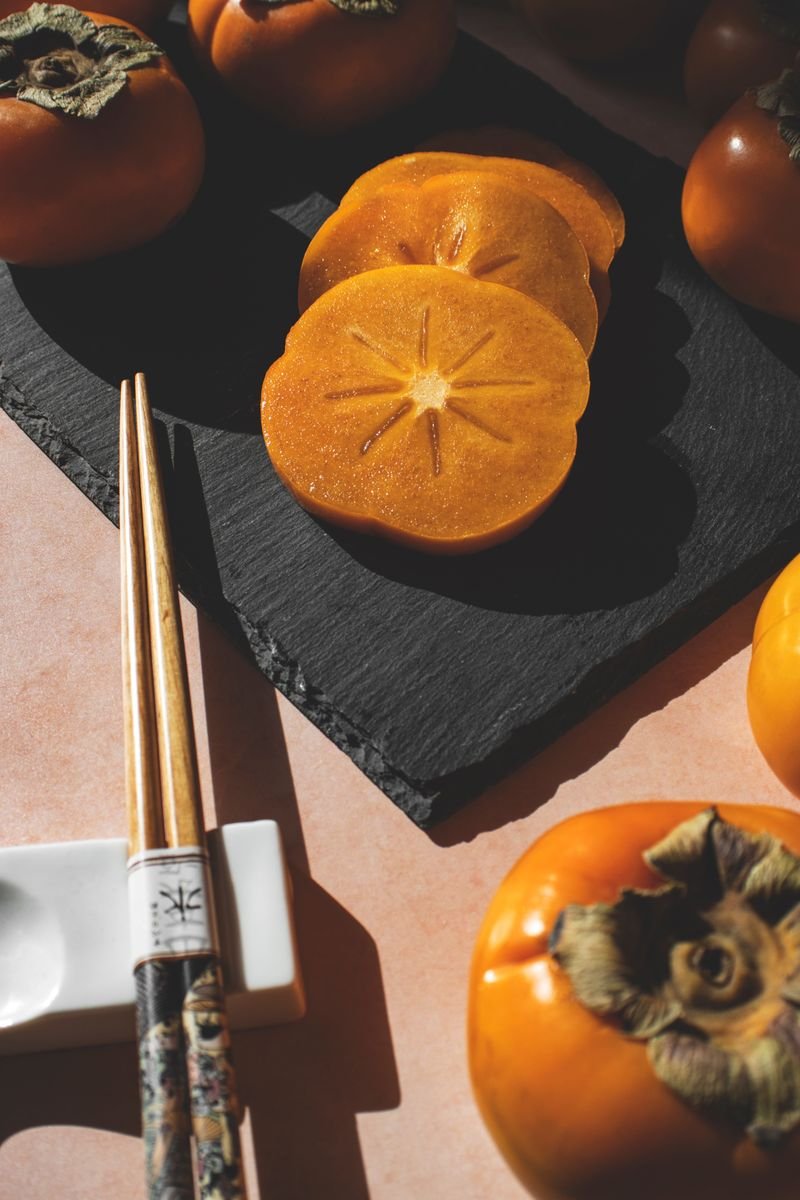 Thin slices of ripe persimmon arranged on a dark slate board with chopsticks
