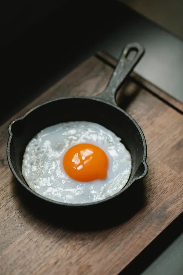 Fried egg cooking in a black cast iron frying pan on a wooden surface