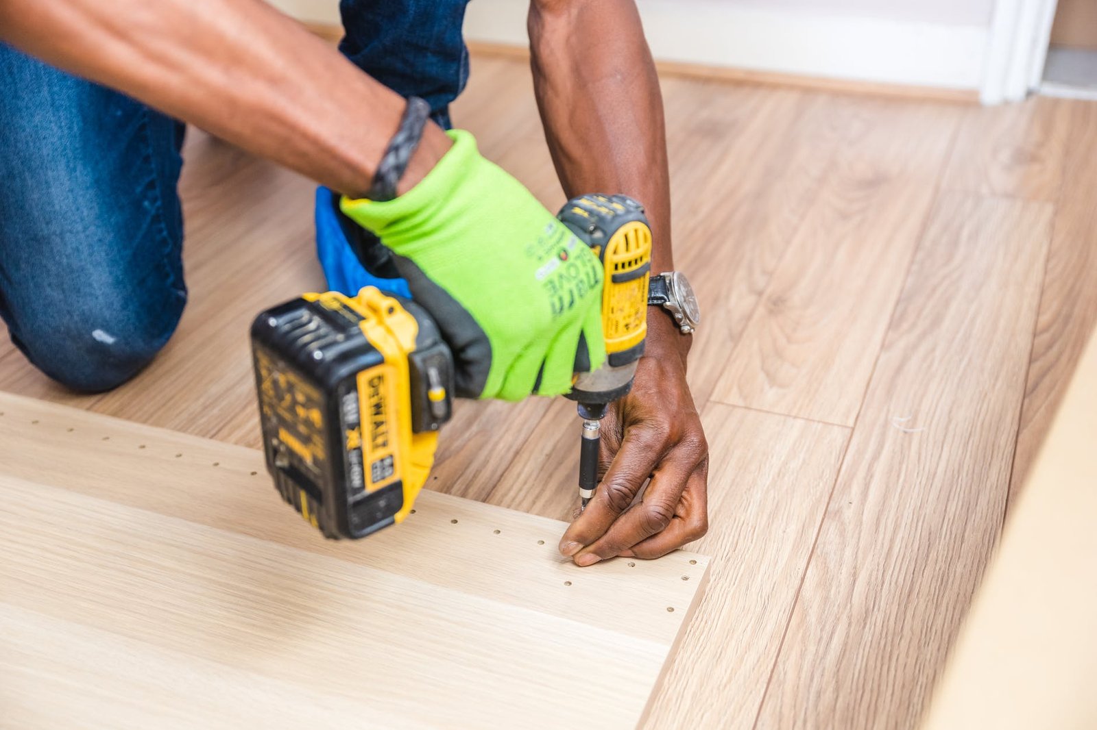 Cordless drill driving a screw through carpet into a floor joist