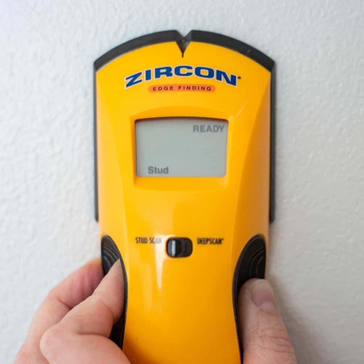 Stud finder held against a wall to locate the timber joist beneath