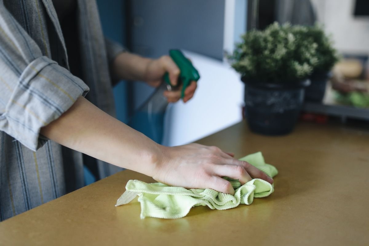 Hand wiping a table with a green microfiber cloth and spray bottle