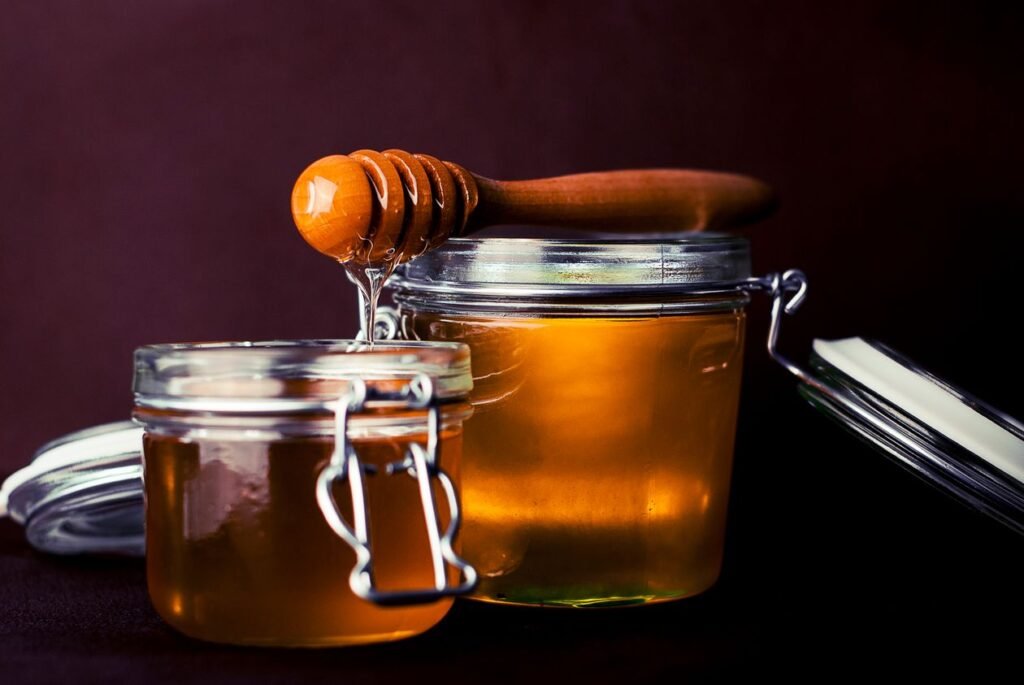 Glass jars of golden honey with a wooden honey dipper on a dark background