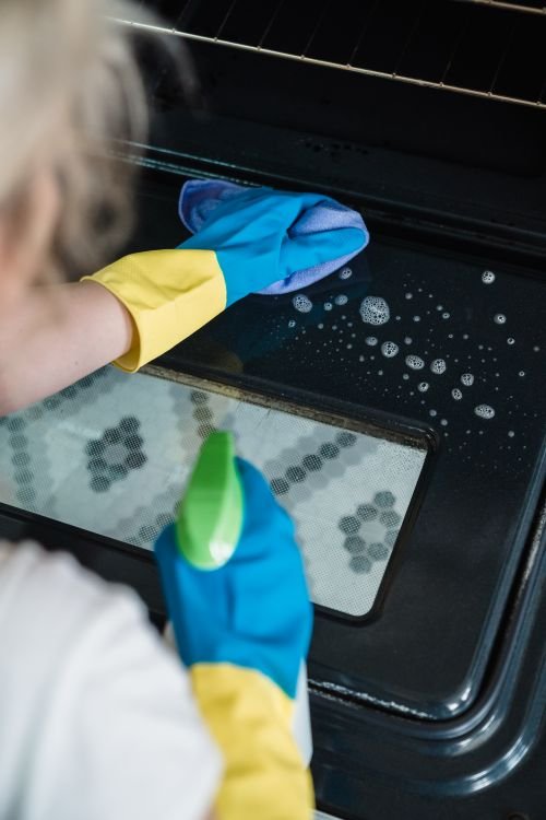 Spraying cleaning solution onto an oven door before wiping it clean
