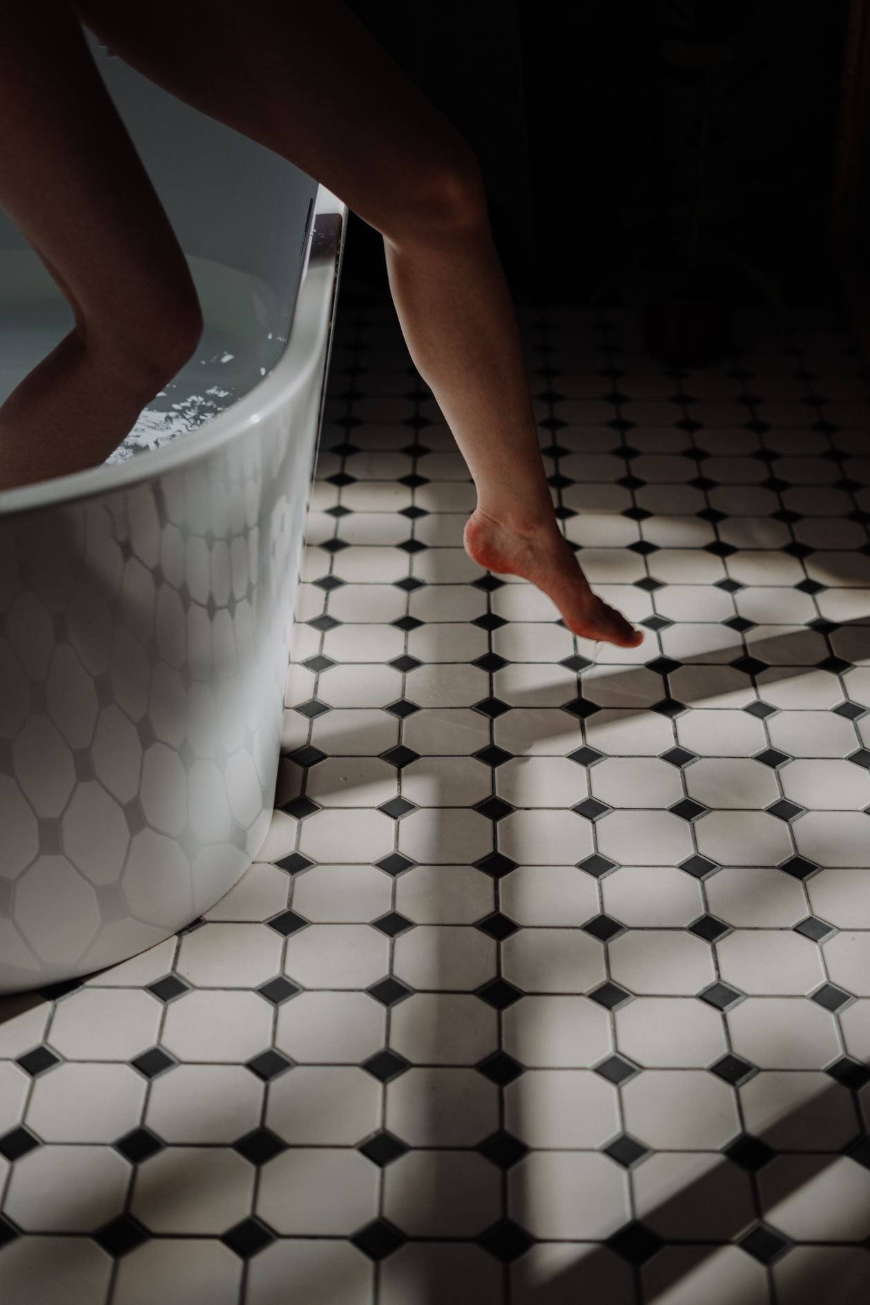 Person stepping into a bathtub in a tiled bathroom