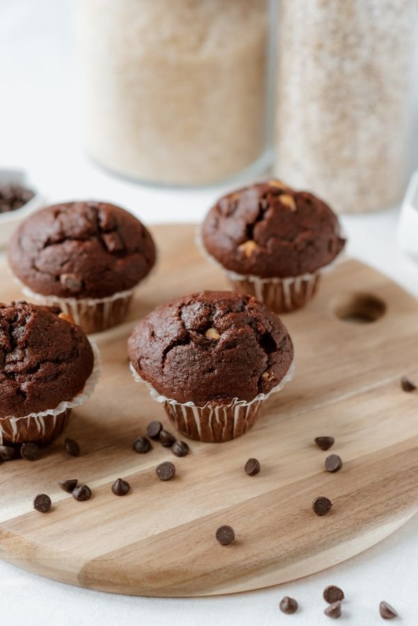 Freshly baked chocolate muffins in paper liners on a wooden board