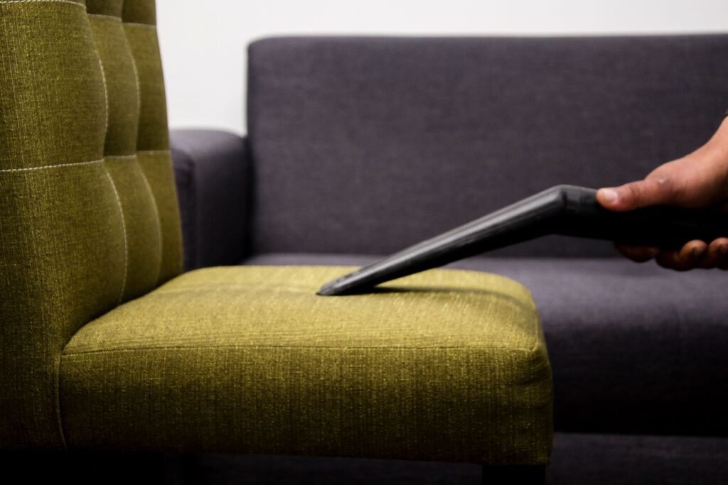 Vacuuming a green fabric chair seat with a narrow crevice tool