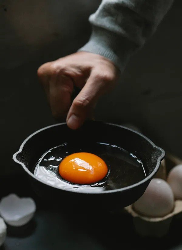 Raw egg just cracked into a hot frying pan with eggshells nearby