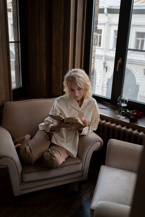 A woman reading a book in a cozy armchair by a tall window, like the memoir in which Miranda Hart shared her health story