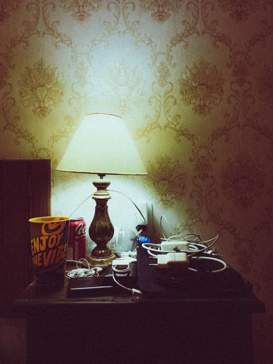 Bedside table at night with a lamp, phone chargers, and charging cables