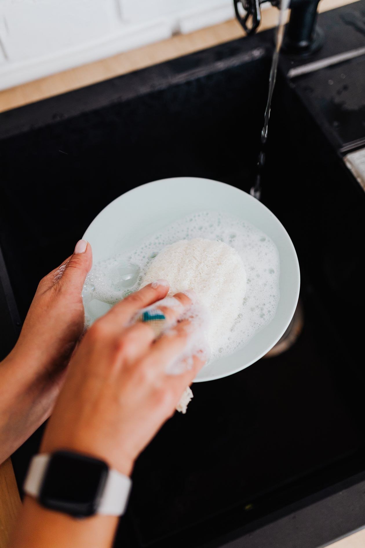 Hands washing dishes with a soapy sponge in a kitchen sink