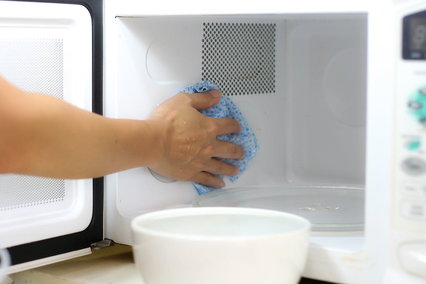 Hand wiping the inside of a microwave with a blue cloth