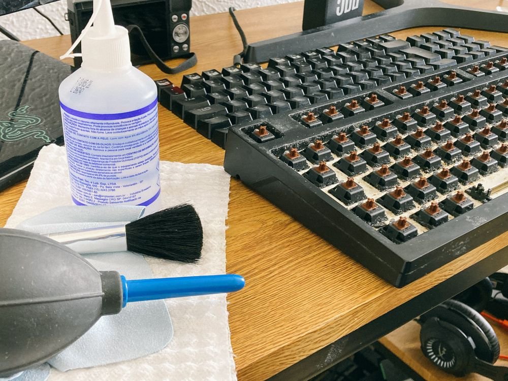 Keyboard cleaning tools including a soft brush, air blower and cleaning solution beside a mechanical keyboard