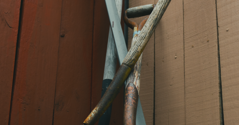 Rusty garden hand tools leaning against a wooden fence before restoration