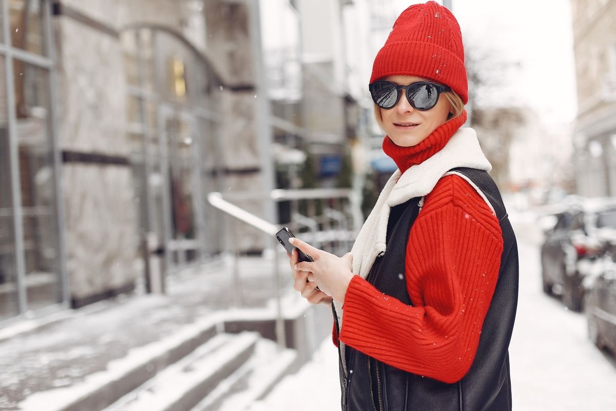 Woman wearing sunglasses in a snowy street shielding her eyes from cold wind