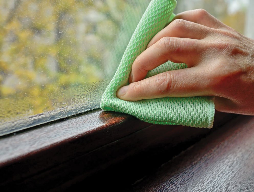 Person wiping morning condensation from a window with a dry cloth